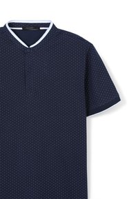 Polo shirt marine avec un motif texturé de points blancs, présentant un col mao et un contraste de finition blanche sur le col et les manches.