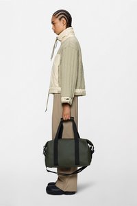 Kurtka pikowana dwukolorowa w odcieniach beżu i oliwkowej zieleni, zestawiona z ciemnozieloną torbą typu duffel z czarnymi paskami i logo.