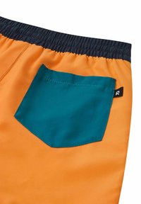 Shorts orange avec une taille élastique, présentant une poche teal à l'arrière. Le tissu semble lisse et léger.
