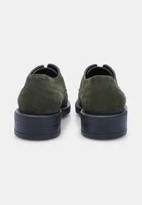 Pantofi din suede verde, cu un design elegant și toc rotund, având o talpă texturată neagră și detalii de cusătură minime.