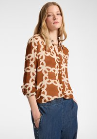 Bruine button-up shirt met een beige in elkaar grijpend kettingpatroon, met opgerolde mouwen en een gladde, zijdeachtige textuur.