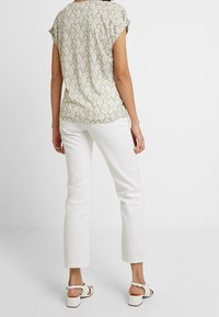 Korte mouwen, lichtgroene blouse met een bladenpatroon, gecombineerd met witte straight-leg broeken en witte sandalen met bandjes.
