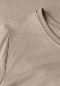 Beige geripptes Material, das einen Nahbereich des Halsausschnitts und der Schulterpartie eines T-Shirts zeigt; zeichnet sich durch eine glatte Textur und fertig verarbeitete Kanten aus.