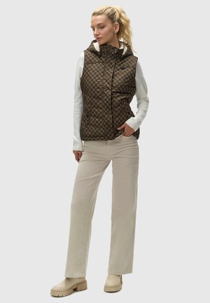 Gilet matelassé à carreaux marron avec une capuche, porté sur une chemise blanche à manches longues, associé à un pantalon en velours côtelé beige et des bottes chunky beiges.