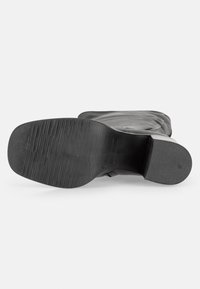 Semelle de botte noire avec grip texturé, forme légèrement incurvée et tige en cuir lisse. Présente un bout arrondi et un design minimaliste.
