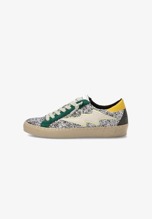 Zapatilla baja con purpurina plateada, ribete verde, diseño de rayo beige, lengüeta amarilla en el talón y suela beige sobre fondo blanco.