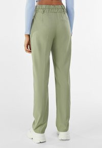 Zielone spodnie o luźnym kroju, z elastycznym paskiem w talii i jedną tylną kieszenią. Tkanina wydaje się gładka i lekka.
