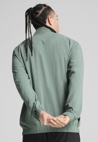 Lichtgroene windjack met elastische mouwen en onderkant. Beschikt over een gladde textuur en een relaxte pasvorm, ontworpen voor comfortabel dragen.