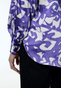 Paars en wit gestreept shirt met een glanzende textuur, voorzien van knopenmanchetten en een ronde zoom. Gepaarde met donkere spijkerbroek.