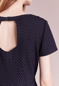Vestido de color navy con mangas cortas, que presenta un pequeño escote en la espalda y un patrón de puntos rojos. Está hecho de una tela suave y texturizada.