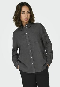 Button-up shirt in dark gray fabric, featuring a collar, long sleeves, and white buttons. Includes a chest pocket and relaxed fit.