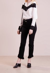 Blusa blanca con acentos negros y cuello con cremallera, combinada con jeans negros de dobladillo deshilachado y mule de piel negras con tacón. Cinturón sencillo y bolso.
