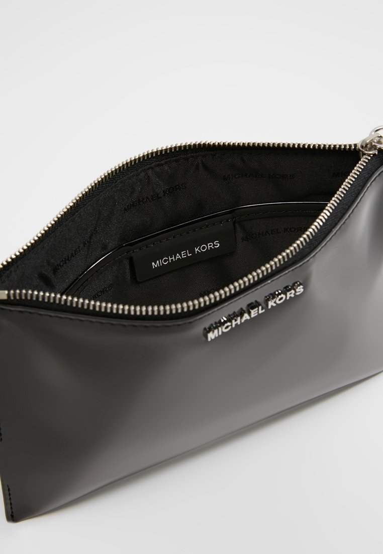 Porte-poignet Michael Kors noir avec fermeture éclair argentée ouverte pour montrer la doublure intérieure de marque et le patch logo en cuir à l’intérieur.