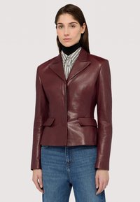 Blazer in pelle bordeaux con revers a punta, due tasche frontali e un design aderente, abbinato a una camicia a righe e denim.