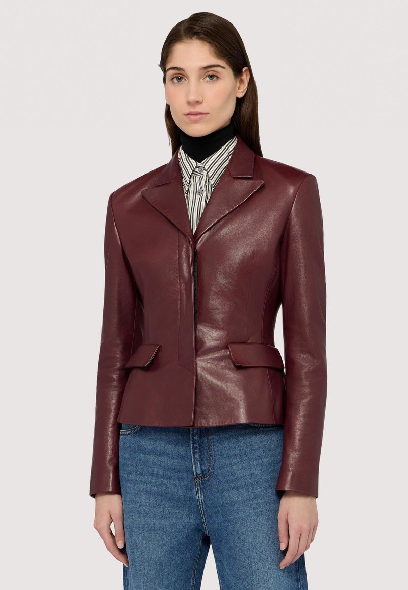 Blazer in pelle bordeaux con revers a punta, due tasche frontali e un design aderente, abbinato a una camicia a righe e denim.