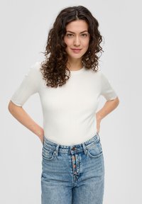 Witte geribbelde top met korte mouwen gecombineerd met hoog-getailleerde vervaagde blauwe spijkerbroeken met een knopenlijst en zijzakken.