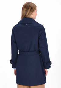 Trenci albastru închis cu talie cu curea, prevăzut cu reveruri late și bretele reglabile la mâneci. Confecționat din material rezistent la apă.