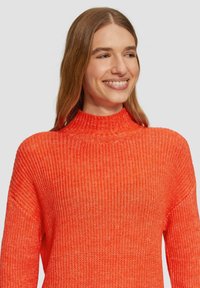 Strickpullover in leuchtendem Orange mit hohem Rippenkragen, lockerer Passform und strukturierten Oberflächen. Verfügt über weite Ärmel und ein lässiges Design.
