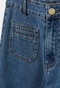 Farkut, joissa on takatasku ja kontrastivärinen ruskea tikkaus. Kangas on keskipitkän sininen ja siinä on hieman haalistunut rakenne.