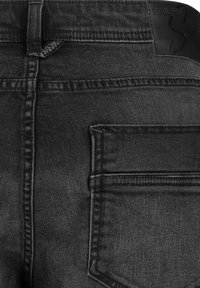 Black denim jeans with a matte texture, featuring a single back pocket and a leather label embossed with "SUBLEVEL." Contrasting stitching details.