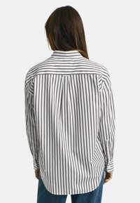 Camicia a maniche lunghe bianca con strette righe verticali rosso scuro, dotata di colletto a punta, polsini con bottone e orlo curvato.