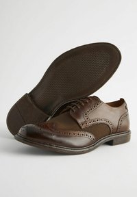 Braune Lederschuhe mit einem Brogue-Design, das mit gemusterten Akzenten und einer strukturierten Gummisohle versehen ist, und einem eleganten, polierten Finish.