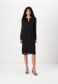 Μαύρο φόρεμα με μακριές διαφανείς μανίκες, κουμπιά μπροστά και φαρδιά φούστα. Συνδυασμένο με μωβ ψηλοτάκουνα σανδάλια. Απλό, κομψό σχέδιο.