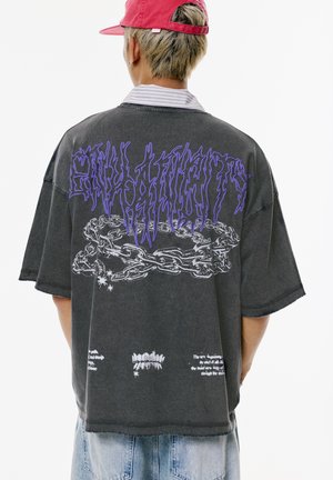 Zwart oversized t-shirt met korte mouwen, voorzien van paarse grafische tekst en kettingen, met een distressed afwerking en extra tekst afgedrukt eronder.