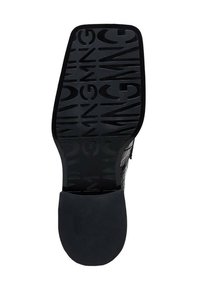 Sålen på en sort dressko med præget gentaget tekst "GIANNI" på forsiden og glat hæl.