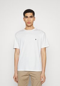 Witte katoenen t-shirt met korte mouwen, ronde hals en klein zwart logo op de borst. De stof lijkt zacht met een gladde textuur.