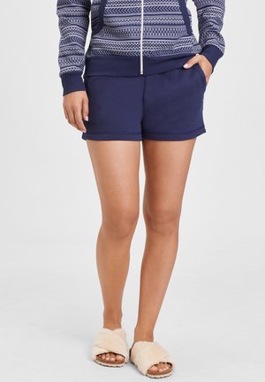 Marineblaue Shorts mit Taschen, aus weichem Material. Warme beige, flauschige Hausschuhe mit offenen Zehen und strukturiertem Fußboden. Minimalistisches Design und legerer Schnitt.