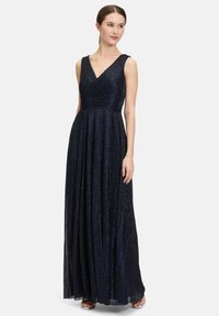 Długa granatowa sukienka wieczorowa z dekoltem w kształcie litery V, fakturowanym materiałem, lekko dopasowanym gorsetem oraz zwiewną spódnicą, zestawiona z srebrnymi sandałami.
