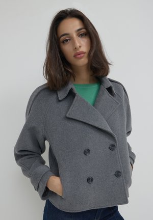 Veste grise à double boutonnage en mélange de laine douce, dotée de grands boutons noirs et d'une coupe décontractée avec des poignets retroussés.