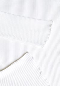 Tejido blanco acanalado con dos piezas superpuestas, que presenta un patrón texturizado a rayas y bordes sin terminar para un estilo casual.