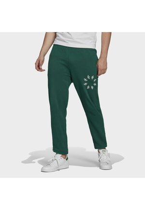 Pantaloni tuta verdi con vestibilità rilassata, caratterizzati da ricami floreali bianchi sulla coscia destra e polsini a costine alla caviglia. Abbinati a sneaker bianche.