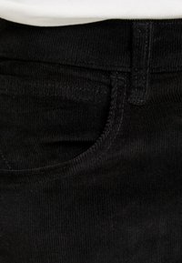 Zwarte corduroy broek met een gestructureerd oppervlak, standaard zakken en een tailleband met riemlussen, die een verticaal ribbelpatroon toont.