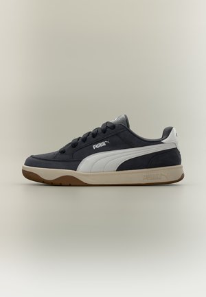 Μαύρο και άσπρο αθλητικό παπούτσι Puma με μπεζ σόλα, σχέδιο με κορδόνια και λογότυπο Puma στο πλάι και στη σόλα, παρουσιασμένο σε ουδέτερο φόντο.