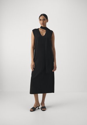 Zwarte mouwloze jurk met een V-hals en zijsplits, voorzien van een draperie in de vorm van een sjaal. Gemaakt van soepele stof met een rechte silhoutte.