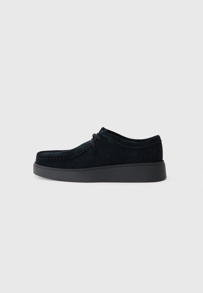 Černá semišová bota s nízkým profilem, kulatou špičkou, jemným prošíváním a gumovou podešví. Nabízí šněrování a minimalistický design.