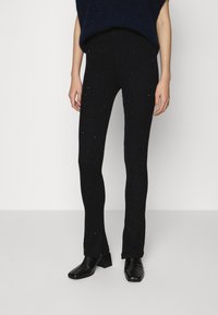 Zwarte geribde gebreide leggings met een subtiele sprankeleffect. Rechte pasvorm met zijsplitten aan de zoom. Gedragen met zwarte gestructureerde hakken.