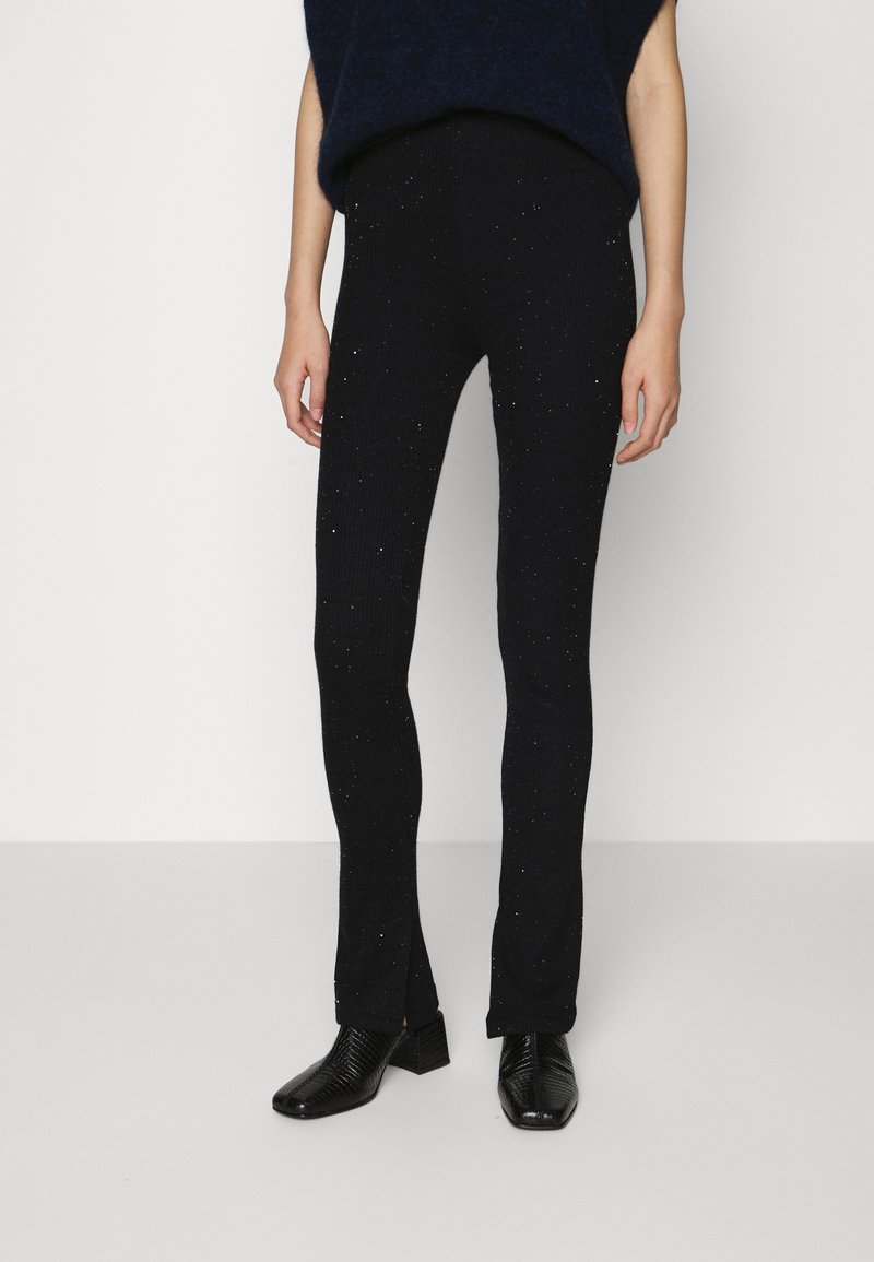 Zwarte geribde gebreide leggings met een subtiele sprankeleffect. Rechte pasvorm met zijsplitten aan de zoom. Gedragen met zwarte gestructureerde hakken.