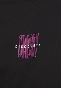 T-shirt noir avec un texte en rose et blanc indiquant "CURIOSITÉ" en arc au-dessus de "DÉCOUVERTE". Tissu doux avec une texture lisse.