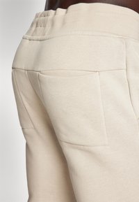Beige bomulls joggebukser med bred elastisk linning og doble lommer bak, med en glatt tekstur og skreddersydd silhuett.