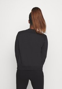Sweat-shirt noir en tissu doux, avec un col rond et des poignets côtelés, coupe décontractée et sans motifs visibles.