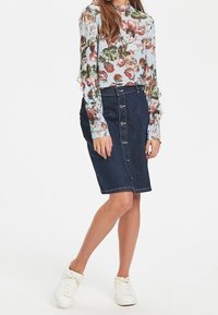 Mörk denim pennkjol med knappstängning fram och sömnadsdetaljer, tillsammans med en ljusblå blommig skjortblus med långa ärmar och vita sneakers.