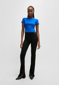 Modrý žebrovaný crop top s krátkým rukávem, spárovaný s černými kalhotami s vysokým pasem a bočními rozparky a černými špičatými botami.
