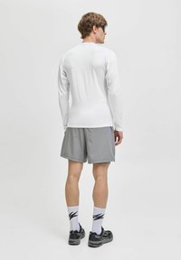 Vit långärmad topp kombinerad med gråa shorts. Texturerad tyg med nätdetaljer på ärmarna, svarta sneakers och mönstrade vita strumpor.