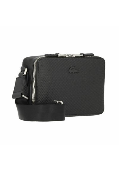 Sac en matériau synthétique noir texturé avec fermeture éclair, bandoulière ajustable et logo embossé sur le devant. Design slim et rectangulaire.