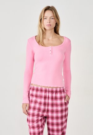Light pink ribbed long-sleeve top with a scalloped neckline and three-button placket, paired with pink plaid pajama pants featuring a loose fit.