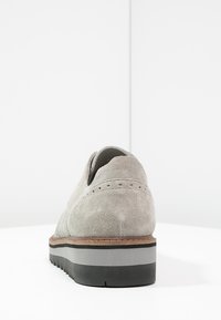 Svetle šedé semišové boty s kulatou špičkou, texturovaným povrchem a kontrastní černou a šedou podrážkou; mají perforované detaily na zadní straně.